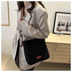 Détail du sac fourre-tout en toile noire avec anses en cuir marron et logo discret