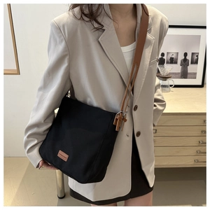 Détail d'un sac cabas en toile noire avec bandoulière en cuir marron et étiquette chic