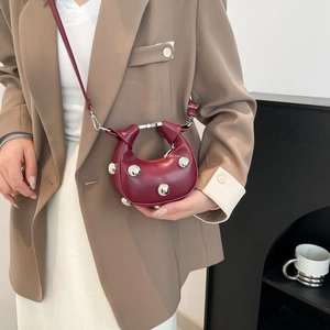 Chic burgundy mini half-moon crossbody bag with silver studs worn by a model