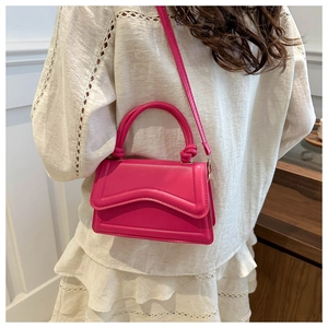 Peach pink crossbody bag with wavy flap detail and braided handle worn by model