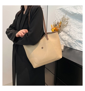 Détail d'un grand sac cabas beige porté par un mannequin en veste de costume noire chic