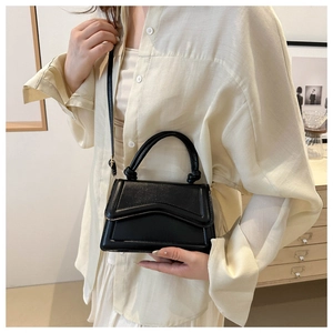 Detailopname van zwarte mini crossbodytas met geknoopt handvat op beige outfit