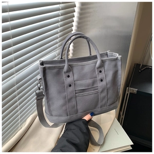Close-up of grey canvas tote bag with adjustable shoulder strap and rivet detailing