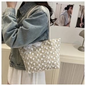 Detail of straw tote bag with white flower lace embroidery and bow ribbon strap