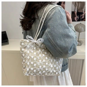Détail d'un sac cabas tissé beige avec broderies florales et grand nœud en dentelle