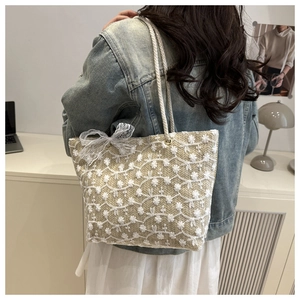 Gros plan détaillé d'un sac cabas en paille beige avec broderie dentelle et nœud blanc
