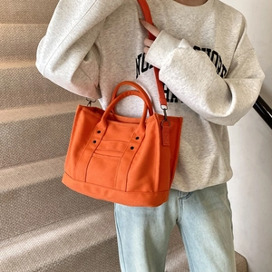 Large orange canvas tote bag with adjustable shoulder straps and stylish rivet details
