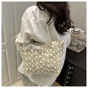 Détail d'un sac bandoulière en paille avec broderie florale et nœud en dentelle blanche