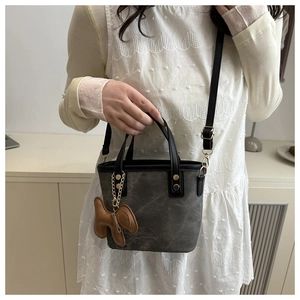 Dark grey canvas and leather bucket bag with puppy charm shown on a white dress