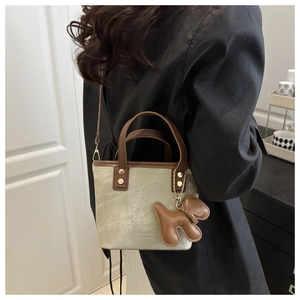 Détail d'un sac seau en toile avec anses en cuir et accessoire breloque chiot marron