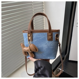 Detail of blue denim bucket bag with brown leather trim and cute puppy charm accessory