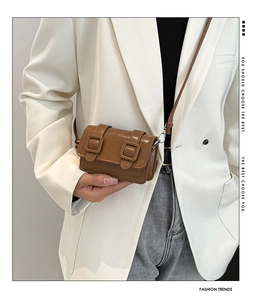 Detail of brown glossy mini crossbody bag featuring vintage double buckle on white blazer