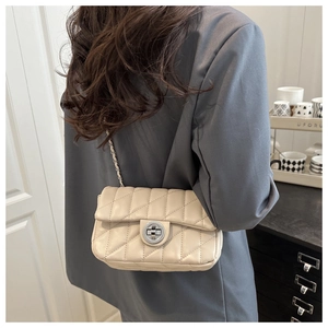 Beige quilted crossbody bag with silver lock worn by a model in a modern interior