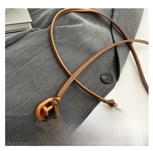 Close-up of brown leather crossbody bag featuring a knotted strap and decorative chain