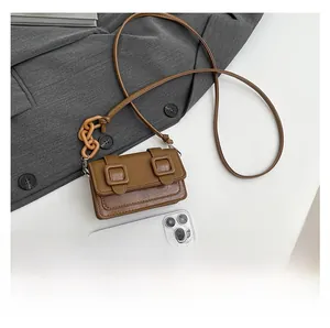 Mini brown crossbody bag size comparison with smartphone showing textured leather detail