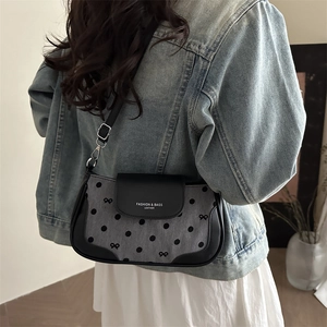 Denim underarm bag with black polka dots and bow pattern shown on a model