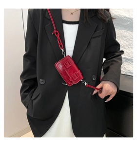Detail of red mini crossbody bag with crocodile texture and resin chain strap on black suit