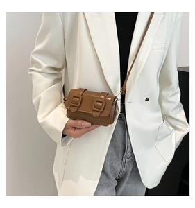Brown mini crossbody bag with metal buckle detail worn over a stylish white blazer