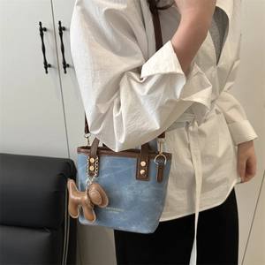 Sac seau en denim bleu et cuir marron porté par un mannequin avec pendentif chien