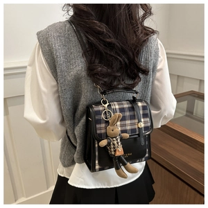 Detail of plaid and black leather backpack featuring a plush rabbit pendant and logo print