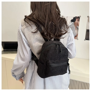 Détail d'un petit sac à dos noir en velours côtelé porté par un mannequin au bureau