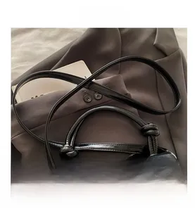 Detail of black leather handbag featuring a unique knotted handle and gold metal buckle