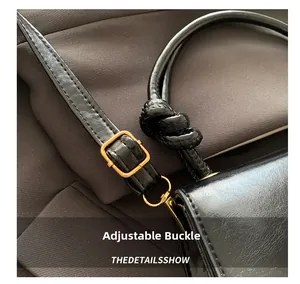 Detail of black pebbled leather shoulder strap with gold buckle and knotted design