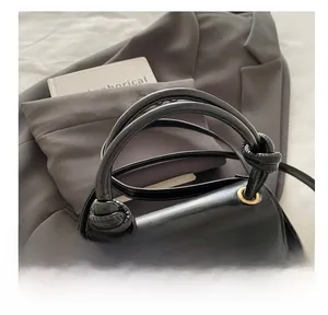 Detail of black patent leather handbag with knotted handle and elegant gold grommet accents