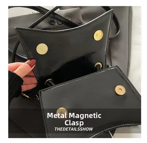 Detailed macro view of the golden magnetic buckle closure on a black leather handbag