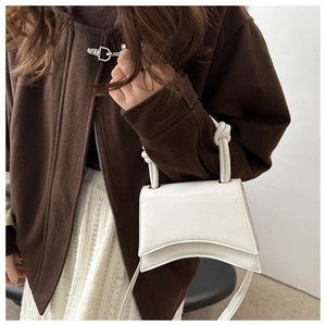 Close-up of white asymmetrical leather handbag with decorative knot on shoulder strap