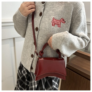 Detail view of dark red glossy leather mini bag with curved bottom and knot handle