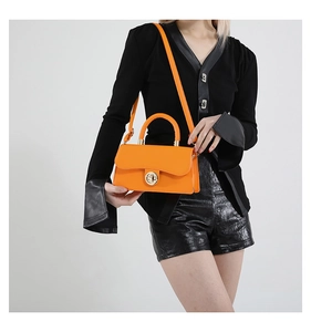 Detail of bright orange handbag with gold twist lock and slim shoulder strap on model