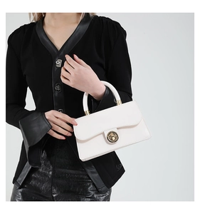 Detail of white leather handbag featuring a round gold metal clasp and a single handle strap