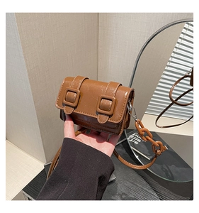 Detail of brown glossy patent leather crossbody bag with chunky chain and square buckles