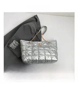 Detail of silver quilted tote bag with golden chain strap and deer charm on grey blazer