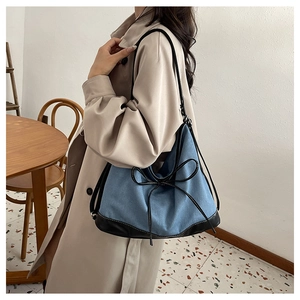 Détail d'un sac cabas en denim bleu avec garniture en cuir noir et nœud décoratif