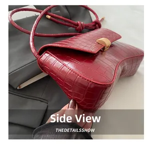 Detail shot of burgundy crocodile pattern leather bag with gold metal clasp closure