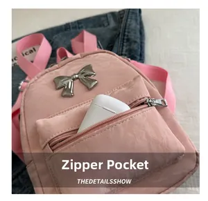 Detailed close-up of pink nylon backpack featuring metal bow and front zipper pocket