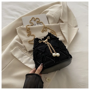 Detail of denim bucket bag with frayed edges, golden chains and large pearl charms
