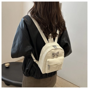 Detailed view of cream PU leather mini backpack with silver bow decoration on black jacket
