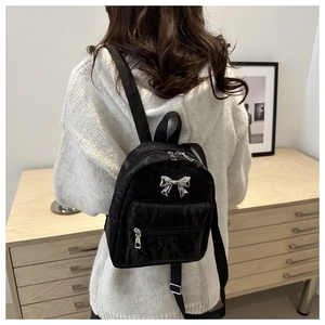 Rear view of a black mini nylon backpack with silver bow detail worn by a model