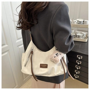 Detail view of cream nylon shoulder bag with brown zipper and plush cat charm accessory