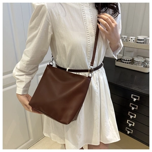 Detail of minimalist dark brown leather bucket bag worn as a retro crossbody style