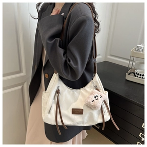 Detailed shot of a white nylon tote bag with brown leather straps and pink plush charm