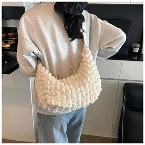 Detail of off-white popcorn texture shoulder bag with soft pleated design in casual setting