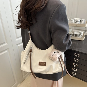 Cream-colored shoulder tote bag with brown straps and cute plush bear charm on a model