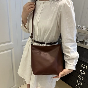 Sac seau minimaliste en cuir marron foncé avec bandoulière réglable porté à l'épaule
