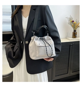 Detail of grey drawstring crossbody bag featuring front flap pocket and woven shoulder strap