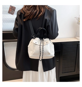 Detail of white drawstring bucket bag with black handle and adjustable shoulder strap