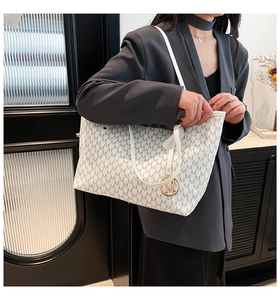 Detail of white tote bag with M-monogram print and golden circular metal pendant charm